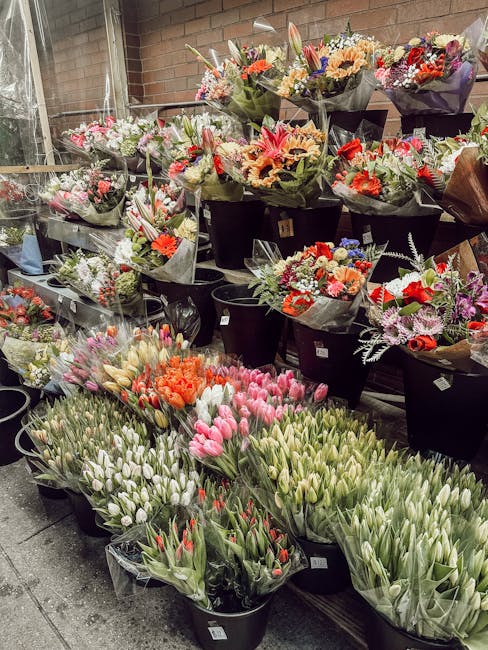 A display of numerous flower bouquets arranged on black buckets, featuring a variety of colorful fresh flowers including pink, white, orange, red, and purple blooms. The arrangements include lilies, t
